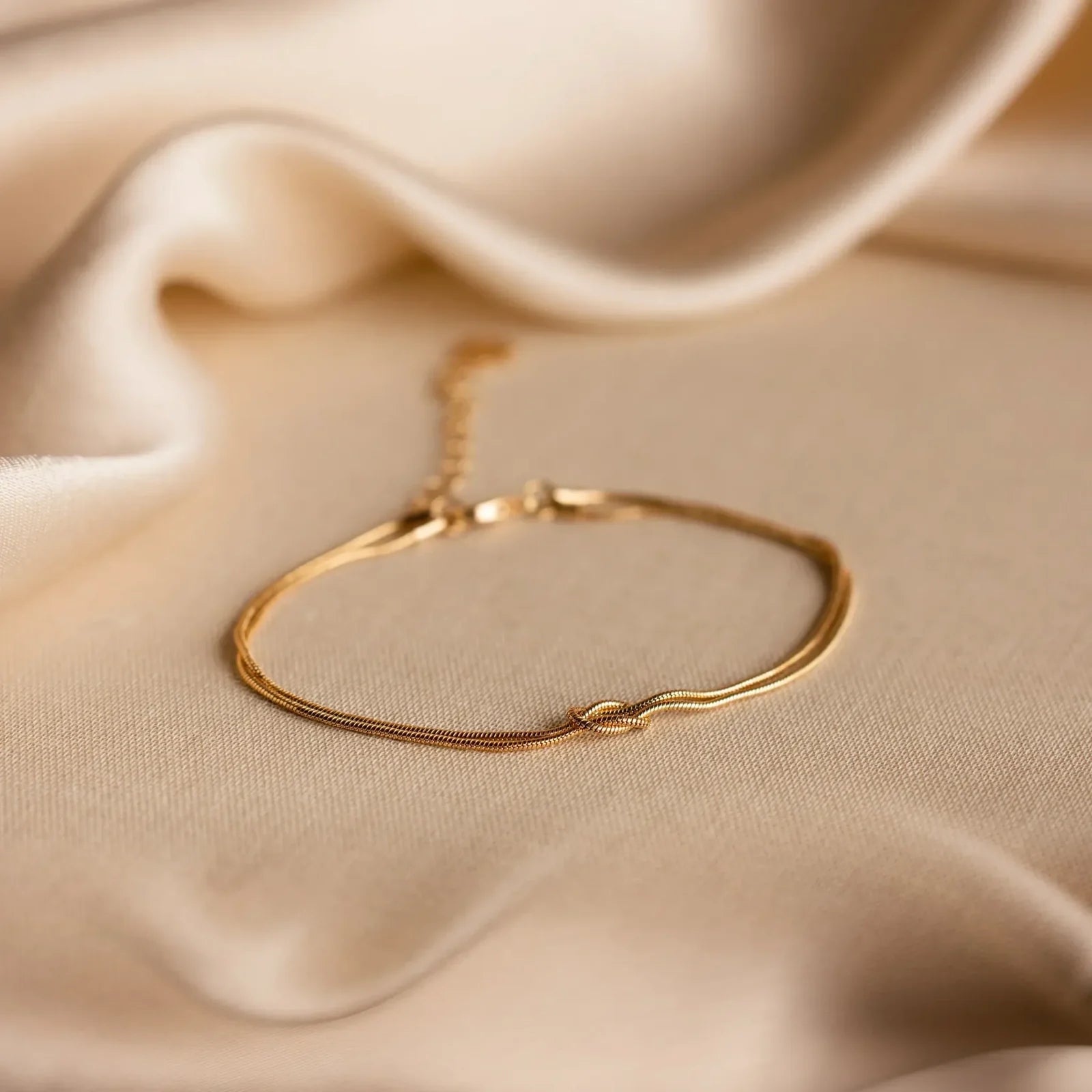 Goldfarbenes Forever Knot Armband auf weichem, cremefarbenem Stoff