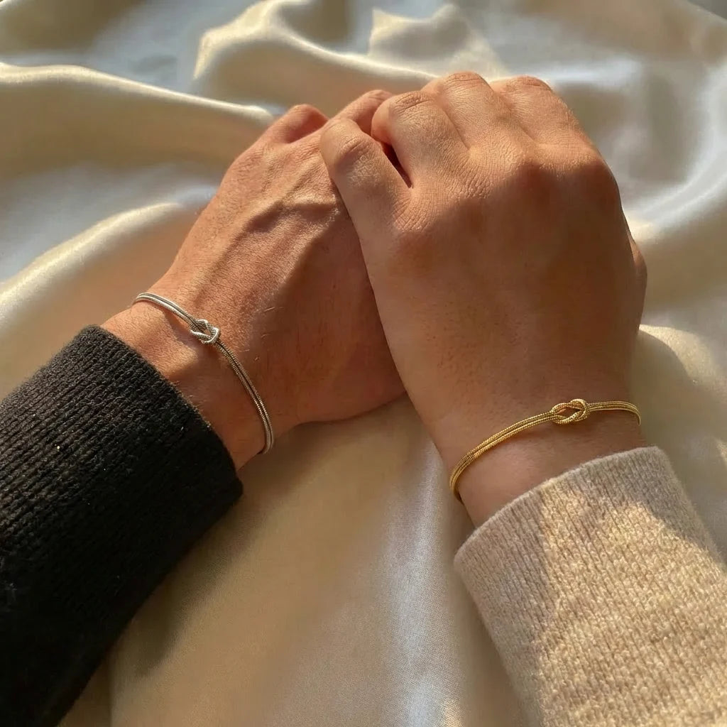 Zwei Menschen legen ihre Hände ineinander, mit einem gold- und silberfarbenen Knotenarmband